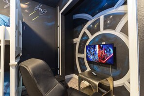 A room with a large screen displaying a movie, a reclining chair, and a wall with a galaxy-themed design.