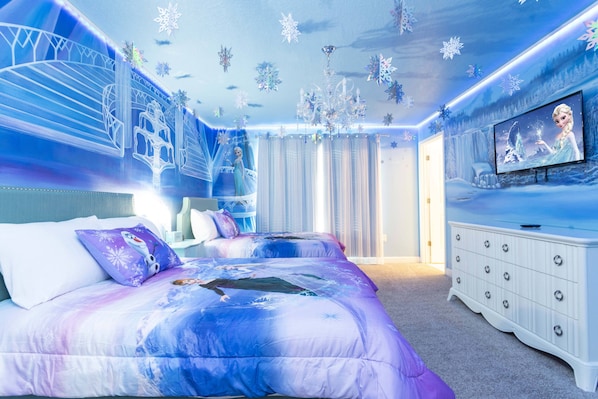 A bedroom with a bed, a dresser, and a television displaying a movie scene.