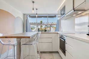 Une cuisine moderne dotée d’une grande fenêtre, de meubles blancs et d’un four encastré.