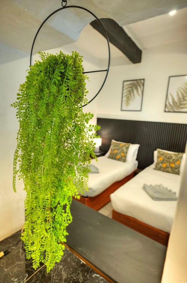 A hanging green plant in a modern hotel room with two beds and a headboard.