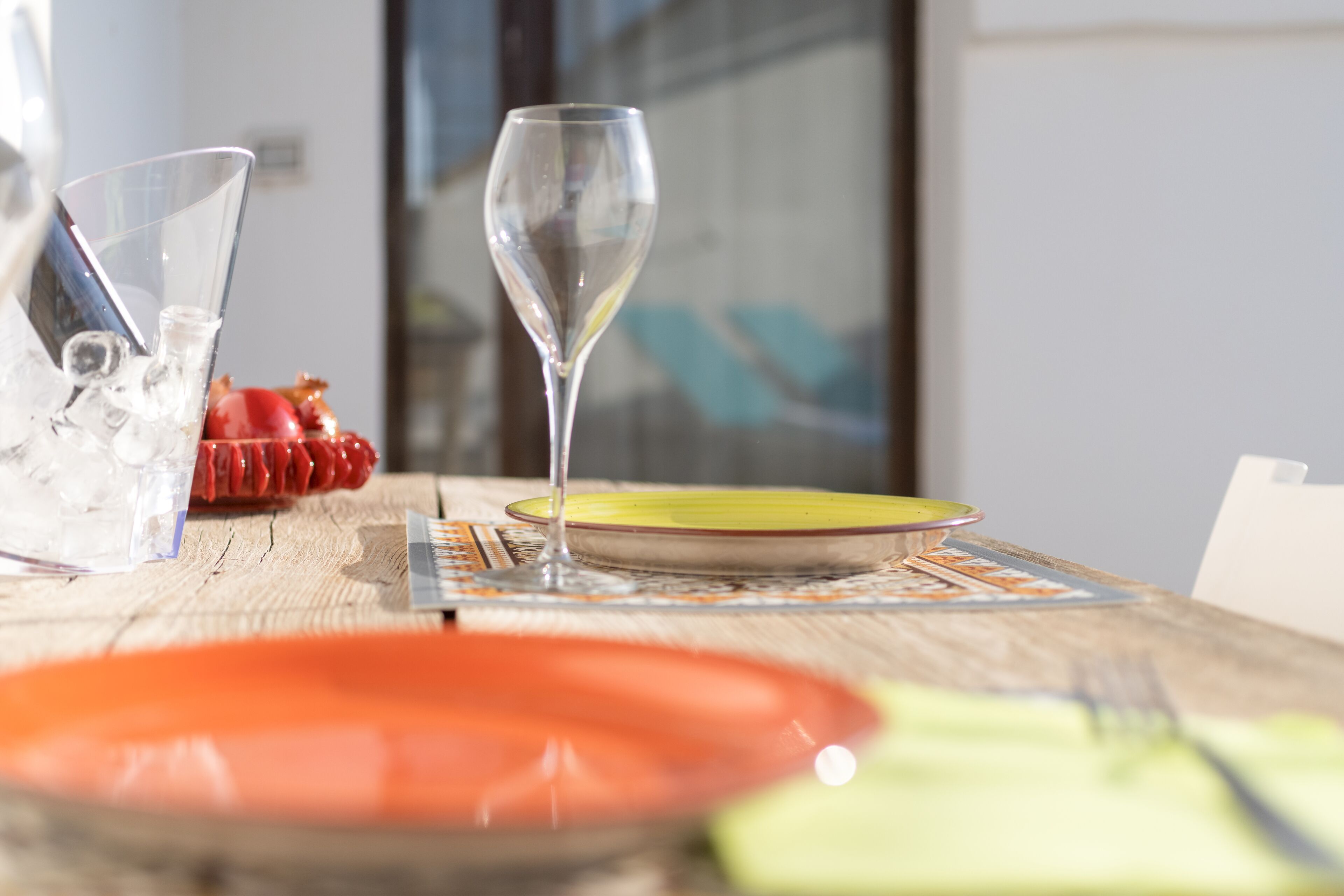 A dining table with a clear glass, a red plate, a yellow plate, and a green plate.