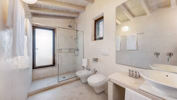 Un bagno moderno con doccia in vetro, un bidet, un water e un ampio lavandino.