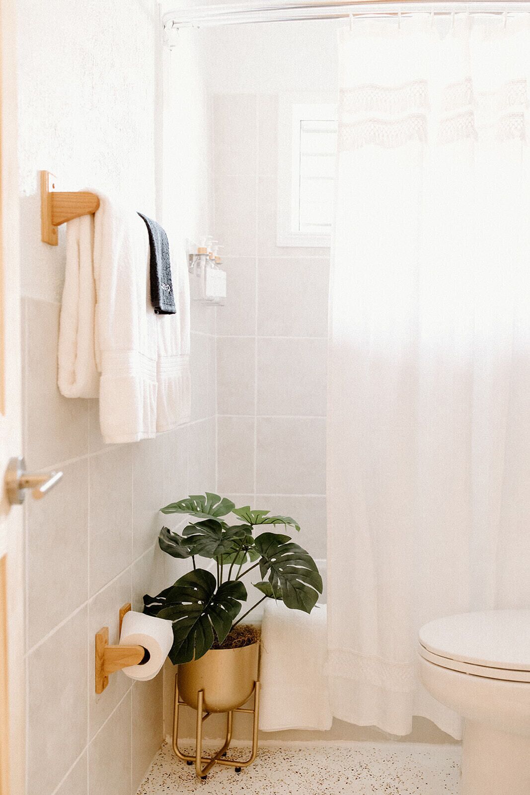 A bathroom with a toilet, a sink, a shower curtain, and a potted plant.