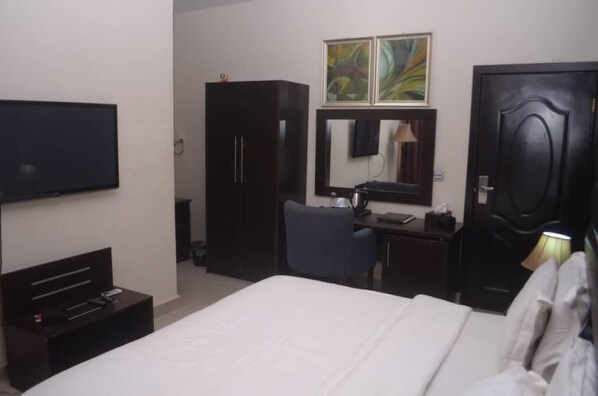 A hotel room with a bed, a desk, a chair, a wardrobe, a TV, and artwork on the wall. - BEGONIA HOTEL LTD  (Oyo)