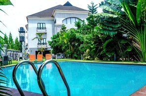 A swimming pool with lounge chairs and a building with balconies in the background. - BEGONIA HOTEL LTD  (Oyo)