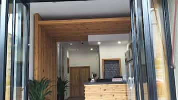 Un área de recepción con mostrador de madera, plantas en macetas y vistas al interior.