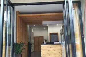Un área de recepción con mostrador de madera, plantas en macetas y vistas al interior.