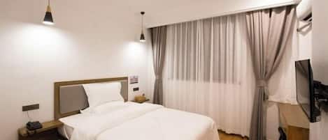 A hotel room with a bed, bedside table, and a desk with a chair.