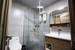 Un baño moderno con ducha envuelta en cristal, inodoro blanco y tocador de madera con espejo.