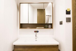 Un baño con lavamanos blanco, un espejo y un mueble de madera debajo.