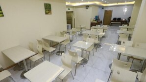 A clean, well-lit dining area with multiple tables and chairs, a tiled floor, and a painting on the wall.