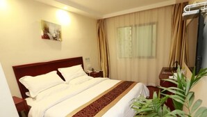 A hotel room with a bed, a nightstand, a lamp, a plant, and a painting on the wall.