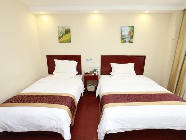 A hotel room with two single beds, each with a wooden headboard, white bedding, and a patterned bedspread. There is a nightstand with a telephone and a small table between the beds. - Greentree Inn Nanjing Jingwu Road Yueyuan Express Hotel (Nanjing)