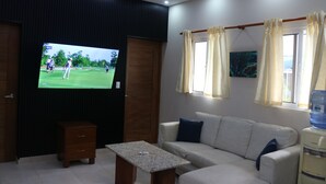 Una sala de estar con televisor de pantalla plana, un sofá, una mesa de centro, un dispensador de agua y una ventana con cortinas.
