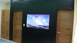 Habitación con un televisor de pantalla plana grande fijado en una pared oscura, flanqueado por puertas de madera.