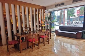 Eine Hotelhalle mit einem Holztisch, roten gepolsterten Stühlen, einem schwarzen Sofa und einem großen Fenster mit Blick auf die Straße.