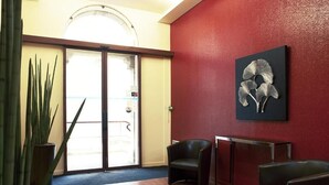 A reception area with a red wall, a black and white artwork, and a potted plant. - Savoy Hotel (Brides-les-Bains)