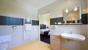 A bathroom with a toilet, a sink, a mirror, and a shower area. - Savoy Hotel (Brides-les-Bains)