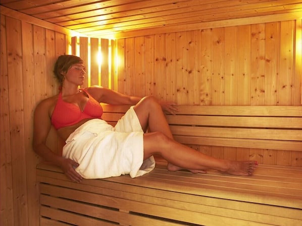 Una persona sentada en una sauna de madera con bancos y paredes de listones.