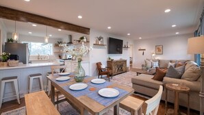 A modern kitchen with a central island, a dining area with a wooden table and chairs, and a living room with a sofa and a TV. - As Featured on Staycation TV, A House, Cottage, & Tiny Home in Downtown Norcross (Norcross)