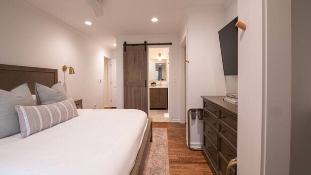 A bedroom with a bed, a dresser, a television, and a kitchen area in the background. - As Featured on Staycation TV, A House, Cottage, & Tiny Home in Downtown Norcross (Norcross)