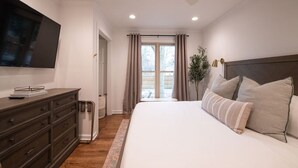 A bedroom with a large bed, a dresser, a TV mounted on the wall, and a window with curtains.