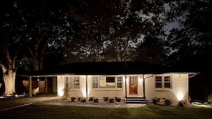 A single-story house with a front porch, a covered garage, and a well-lit exterior at night.