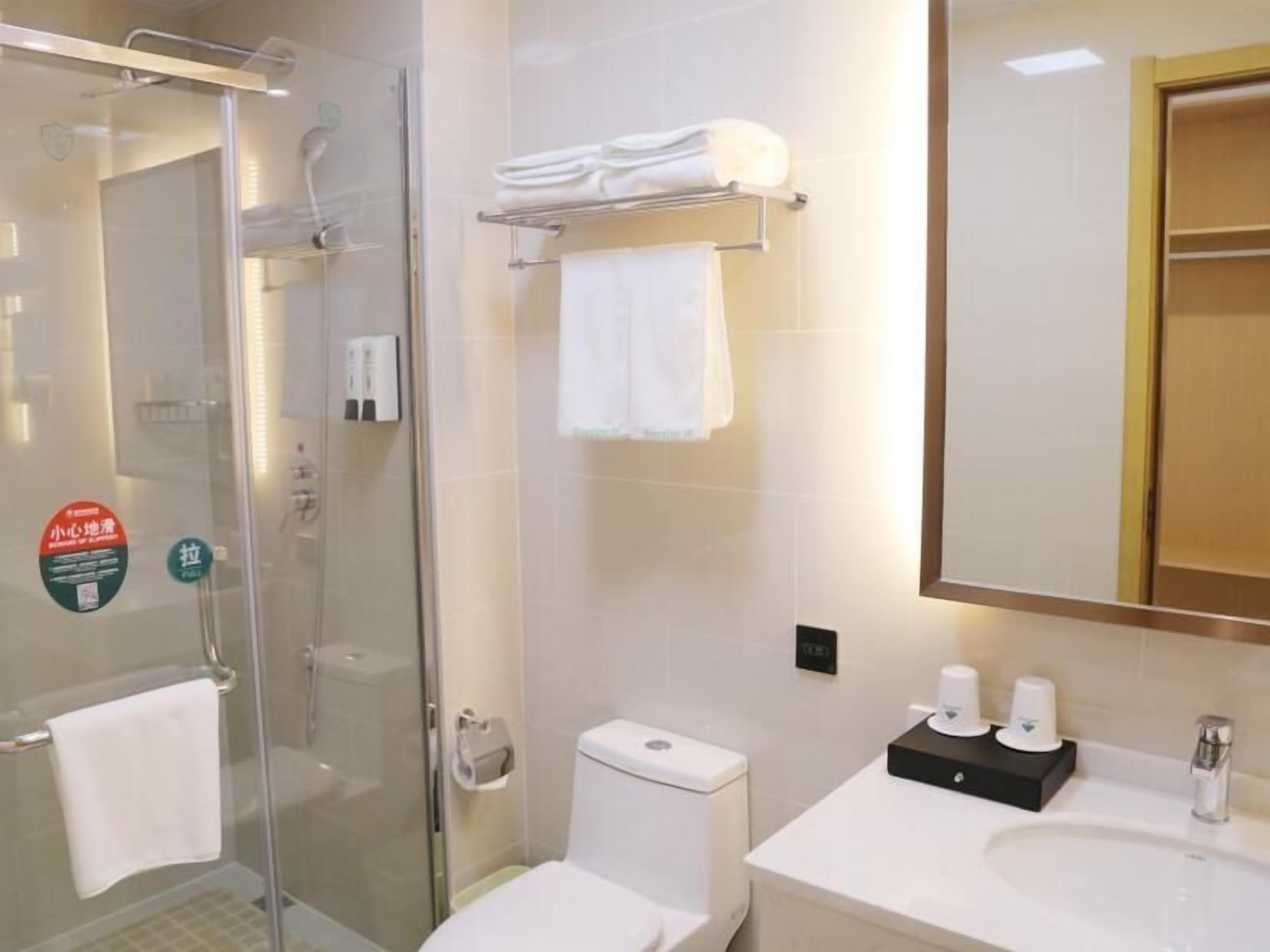 Un baño moderno con cabina de ducha de vidrio, inodoro, lavamanos con espejo y toallero.