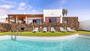 Una casa moderna con piscina, muro de piedra y sillones blancos.