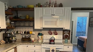 A kitchen with white cabinets, a stove, a microwave, and a dining area with a wooden table and bench.