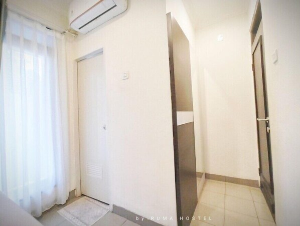 A hallway with a closed door, a small window with sheer curtains, and a tiled floor. - Ruma Hostel (Bandung)