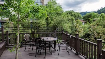 A wooden deck with a round table and chairs, surrounded by a wooden railing, overlooking a lush green landscape.