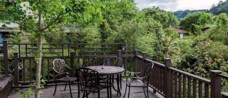 A wooden deck with a round table and chairs, surrounded by a wooden railing, overlooking a lush green landscape.