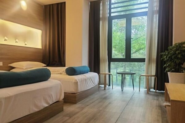 A hotel room with a large window, a bed with white bedding and blue pillows, a small table, and a chair. - Wuyishan Qianyishanshe Villa (Wuyishan)
