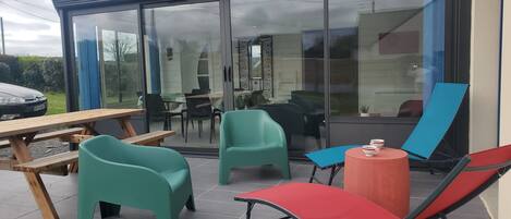 Une terrasse extérieure avec une porte vitrée donnant sur un coin repas, une table de pique-nique et plusieurs chaises.