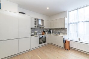 A modern kitchen with white cabinetry, a built-in oven, a microwave, and a window providing natural light. - Luxury hot tub Family/dog Friendly bungalow-garden (Appleby - In - Westmoorland)
