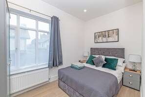 A bedroom with a bed, bedside tables, a window with curtains, a radiator, and a painting on the wall. - Luxury hot tub Family/dog Friendly bungalow-garden (Appleby - In - Westmoorland)
