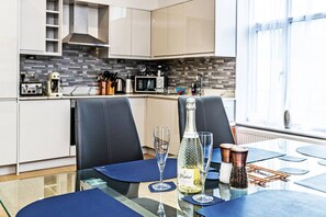 A modern kitchen with a glass table set for dining, a bottle of champagne, and a salt and pepper shaker.
