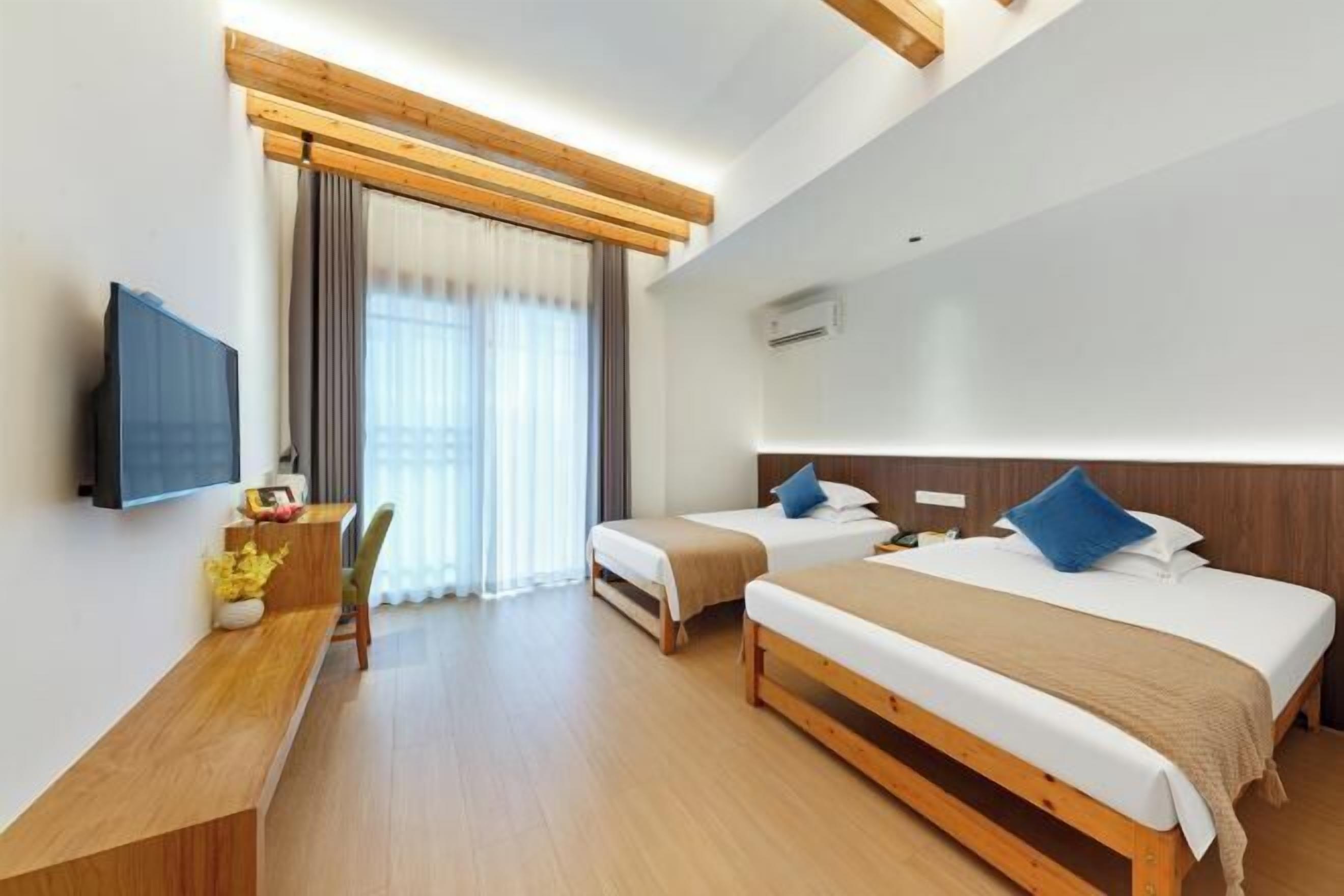 Une chambre d’hôtel avec deux lits, un bureau, une télévision et une fenêtre avec des rideaux.