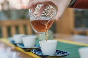 Een hand schenkt een vloeistof uit een gestructureerd glas in een witte kop op een schotel.