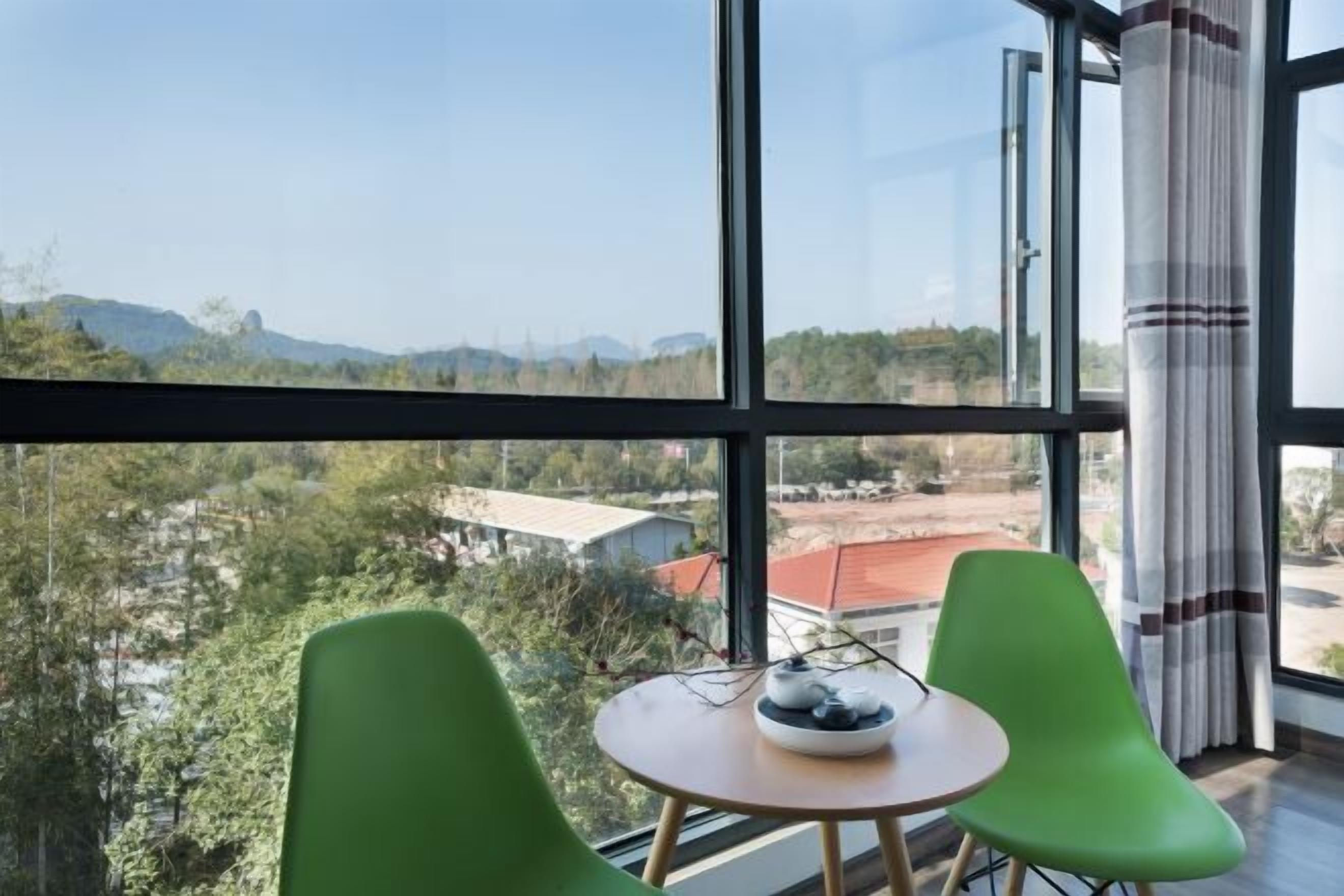 A room with large windows, a round table, and two green chairs.