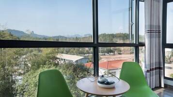 A room with large windows, a round table, and two green chairs.