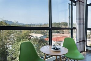 A room with large windows, a round table, and two green chairs. - Xingwan Tianranju（South Entrance of Wuyi Mountain National Park） (Wuyishan)
