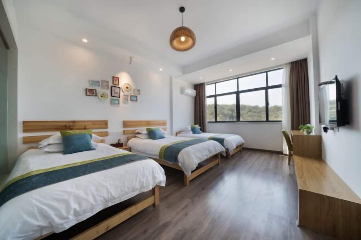 Habitación de hotel con tres camas individuales, un escritorio de madera, televisión y un ventanal con vistas al exterior.
