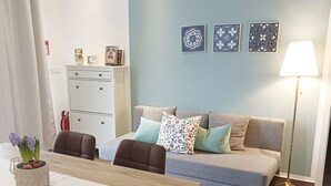 Uma sala de estar moderna com uma mesa de jantar de madeira, cadeiras estofadas em tons de castanho, um sofá cinza com almofadas estampadas e um abajur.
