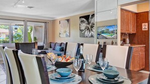 A dining area with a table set for four, a sofa, and a kitchen area with wooden cabinets. - Heated Pool-Waterfront 4BD Villa: Deck&BBQ (Fort Lauderdale)