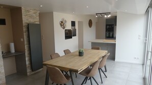 A modern dining area with a wooden table and four chairs, a small potted plant, and a kitchen in the background. - House Townhouse with terrace and enclosed garden near town center (Talmont-Saint-Hilaire)