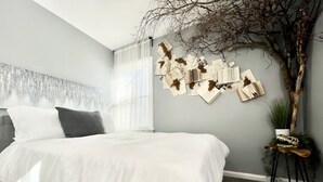 Un dormitorio moderno con una cama grande, una decoración de rama de árbol y una pared con papeles y fotografías.