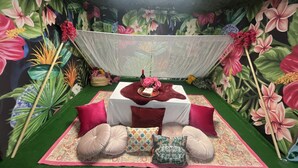 Una habitación con piso de césped artificial verde, una mesa blanca cubierta con un paño rojo y una variedad de almohadas.