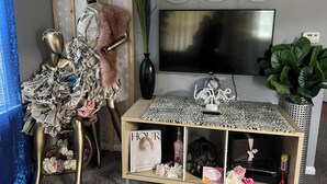 Una sala de estar con televisor, una estantería decorativa con libros y flores, un maniquí y una pared con adornos con forma de boca.